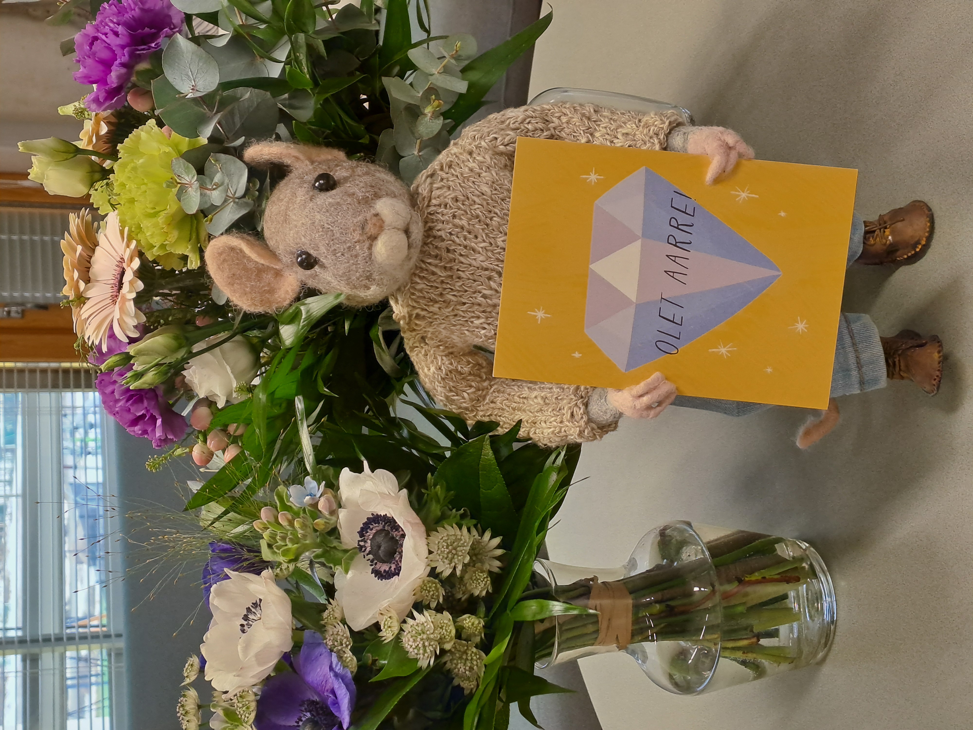 Koulun maskotti Hipsu-hiiri kukkien ja onnittelukortin kanssa.