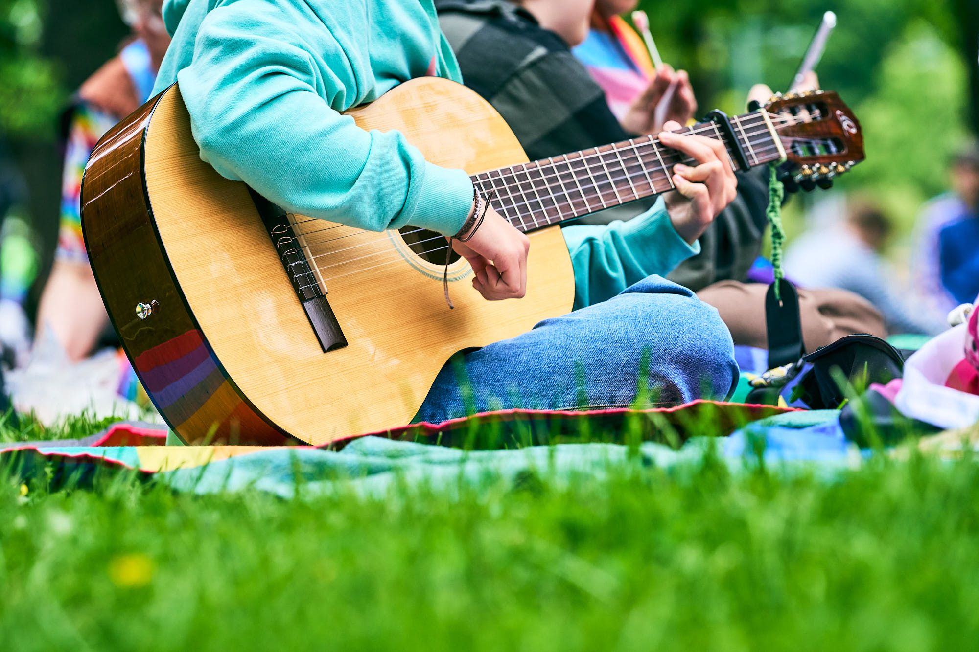 Lähikuva henkilöstä soittamassa kitaraa nurmikolla.