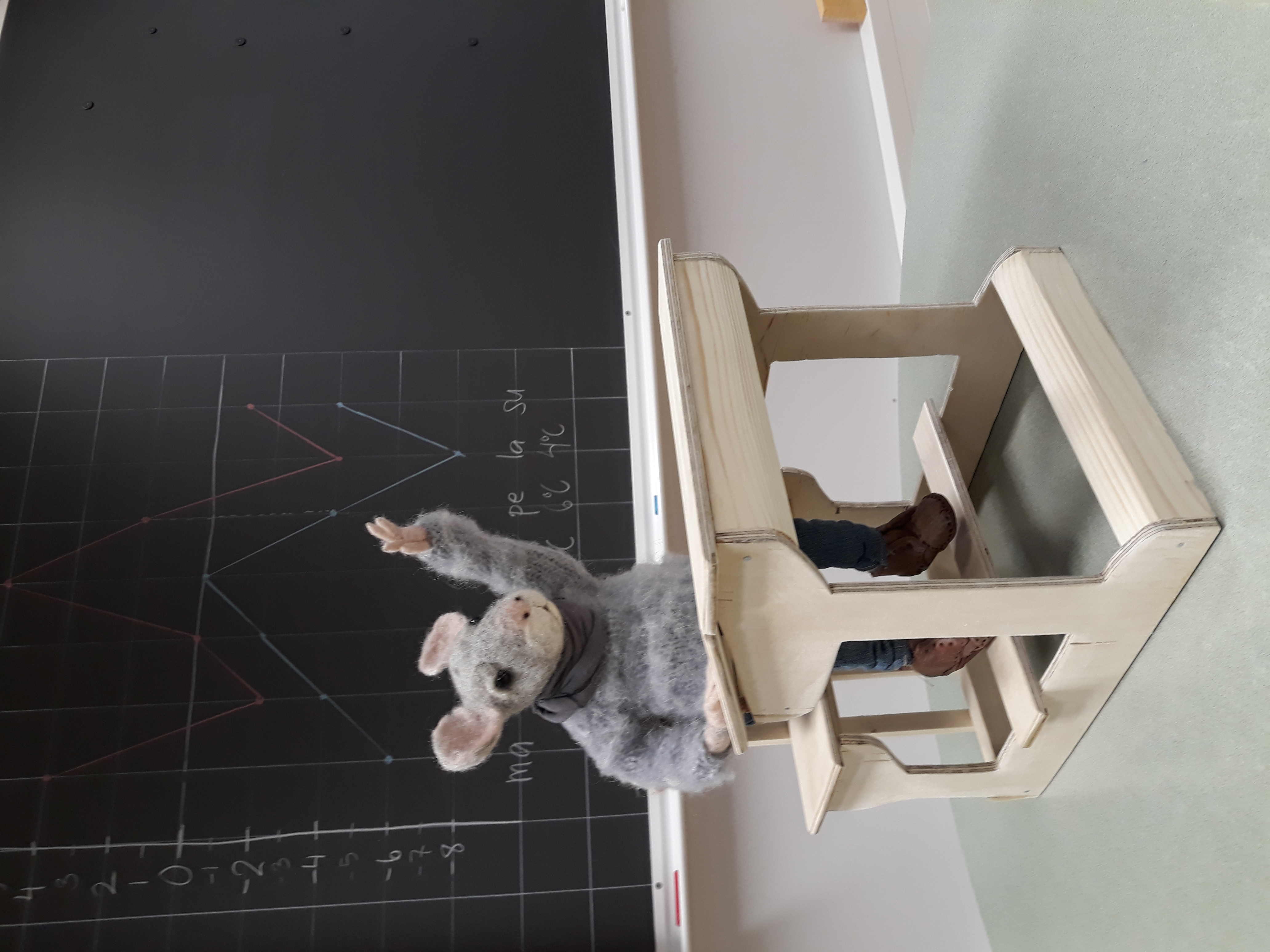 Koulun maskotti Hipsu-hiiri istuu pulpetin ääressä ja viittaa.