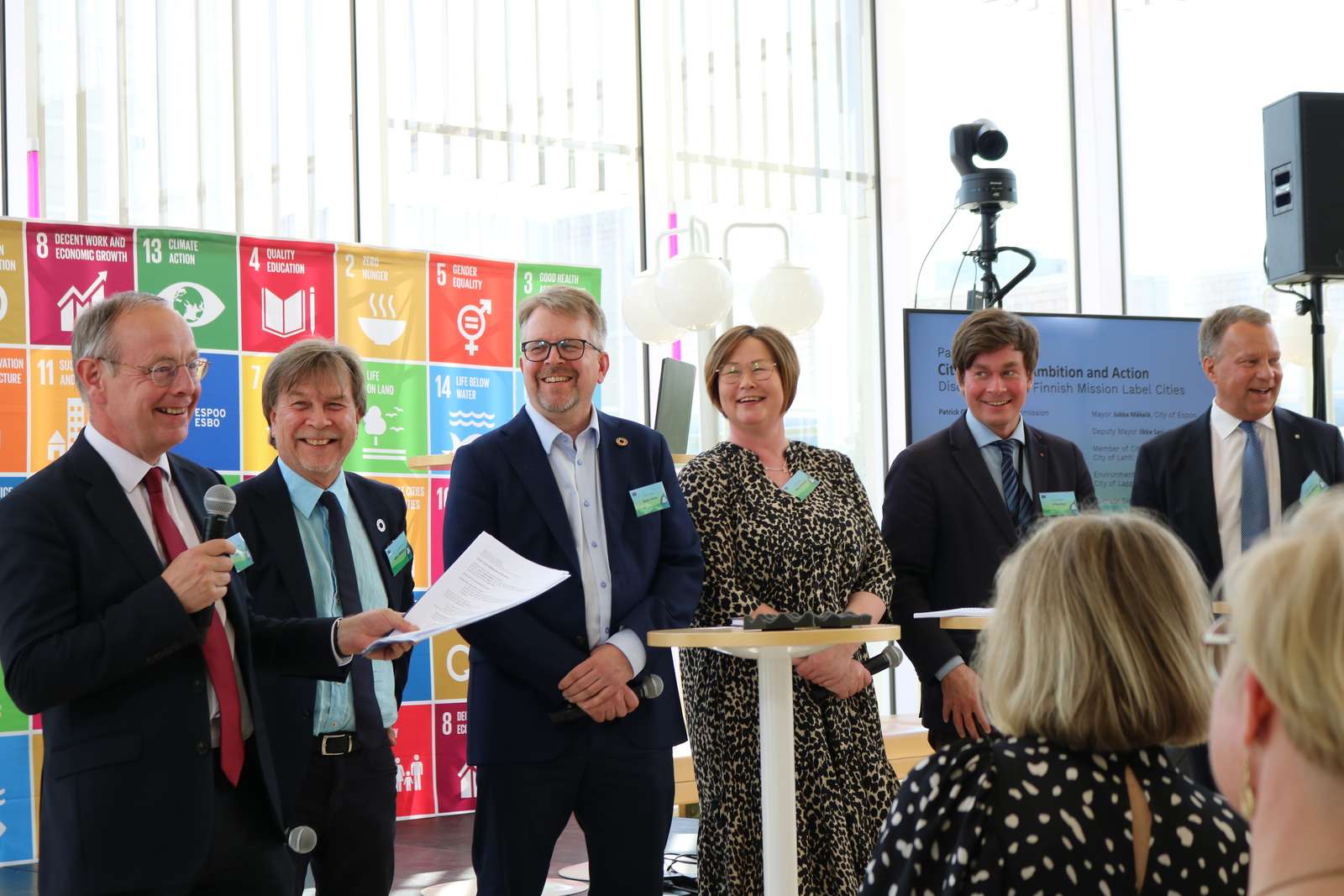 Kuusi ihmistä lavalla hymyilee toisilleen.