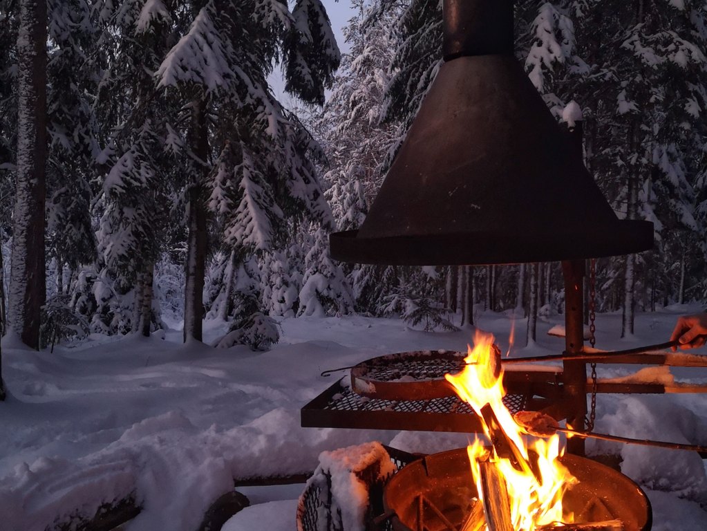 Luminen talvimaisema luonnossa, etualalla nuotio ja tuli.