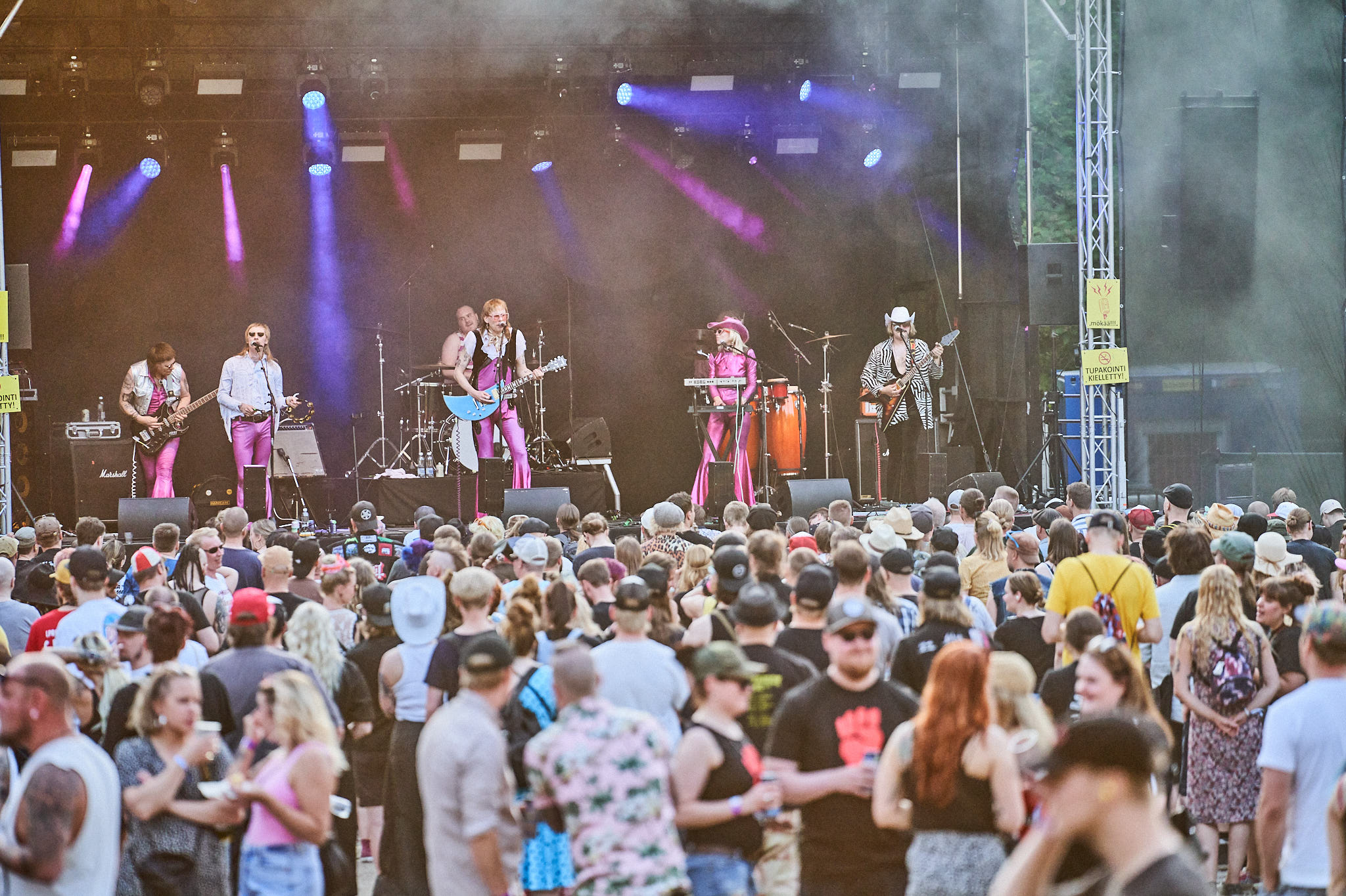 Joukko ihmisiä seuraa lavalla olevan bändin keikkaa kesäpäivänä.