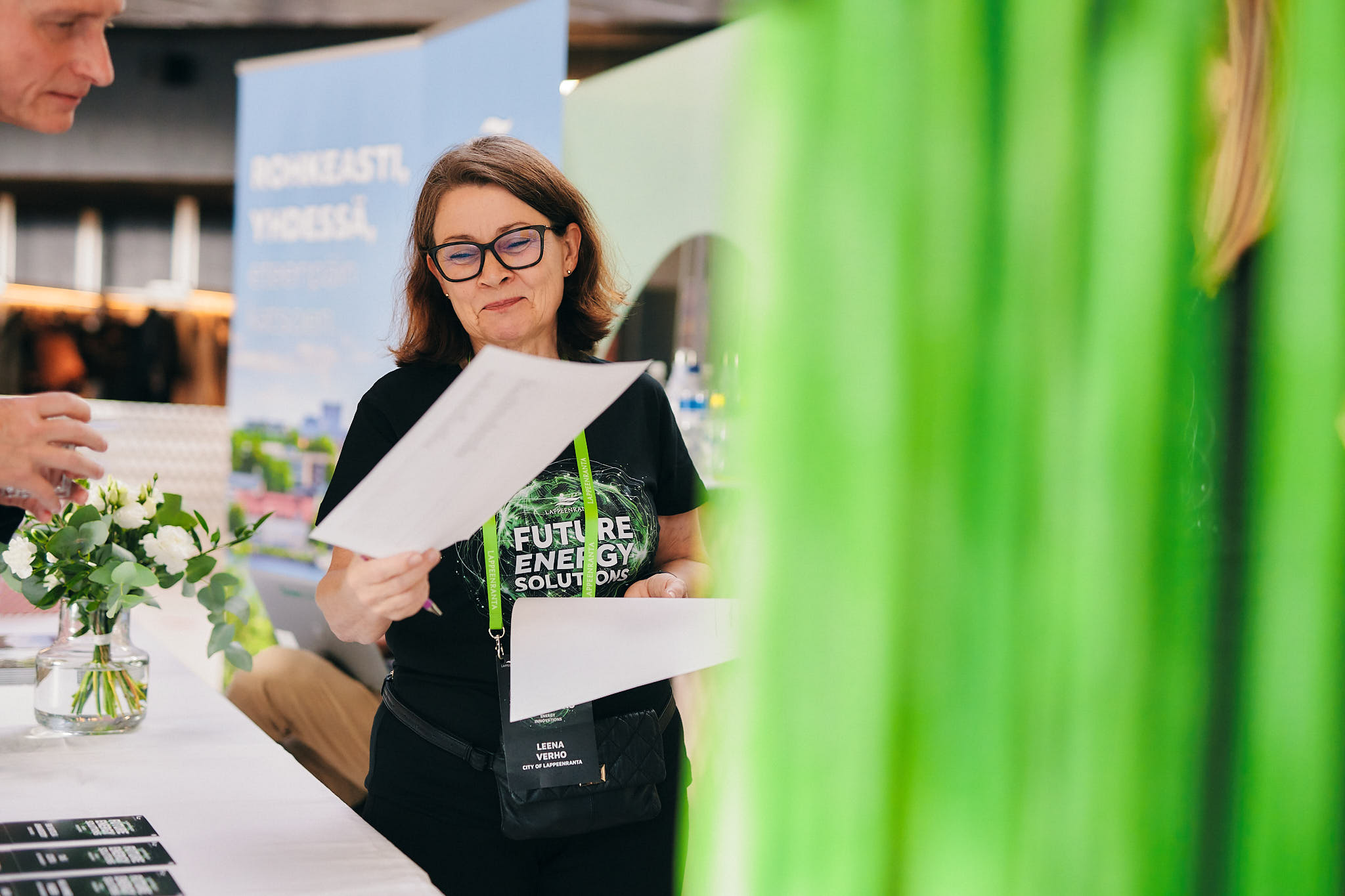 Hymyilevä nainen esittelee käsissään olevia papereita.