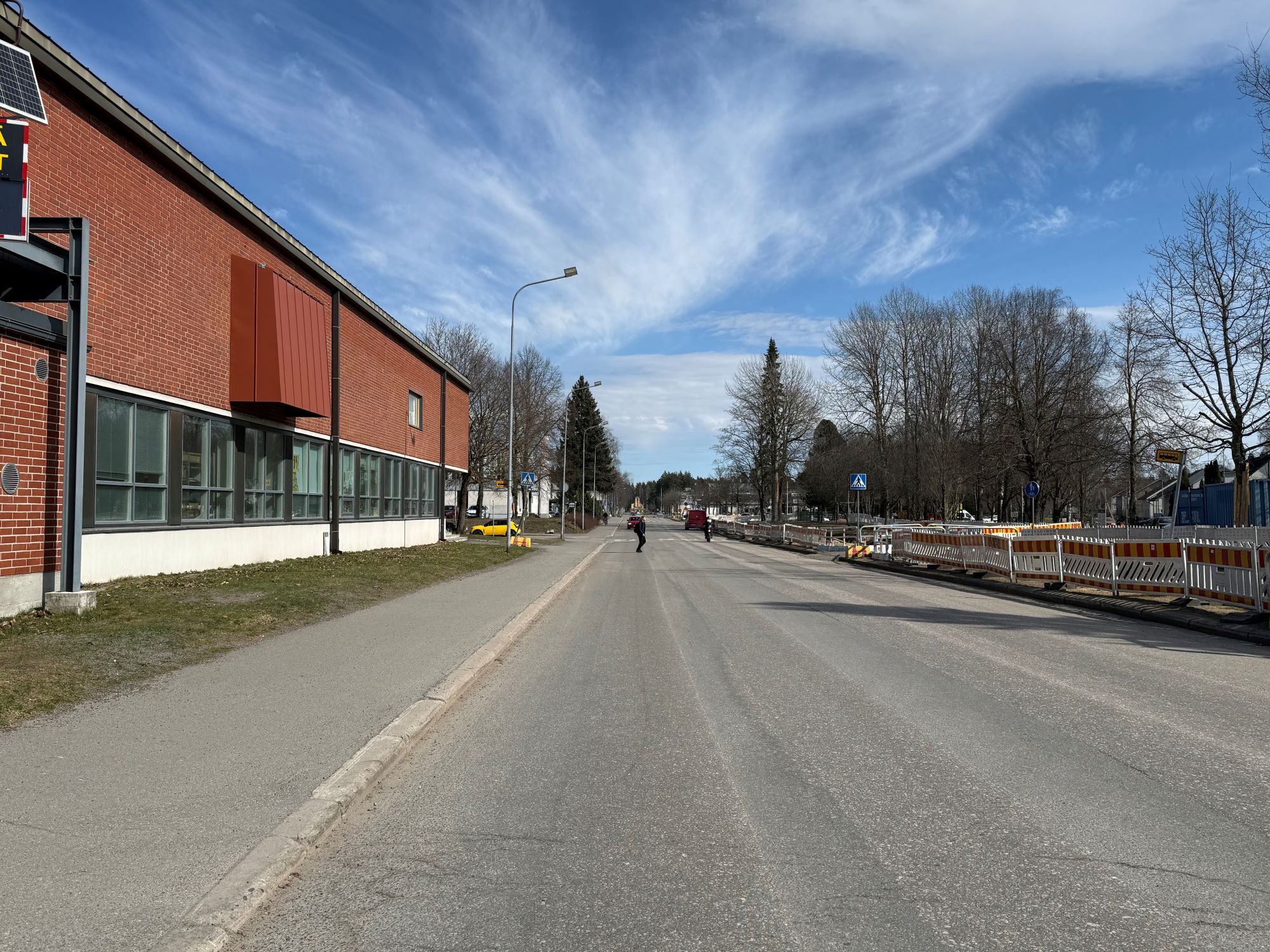 Armilankatua, jossa pyörätie ja koulurakennus vasemmalla, oikealla työmaa-aitoja. Puita tien varrella.
