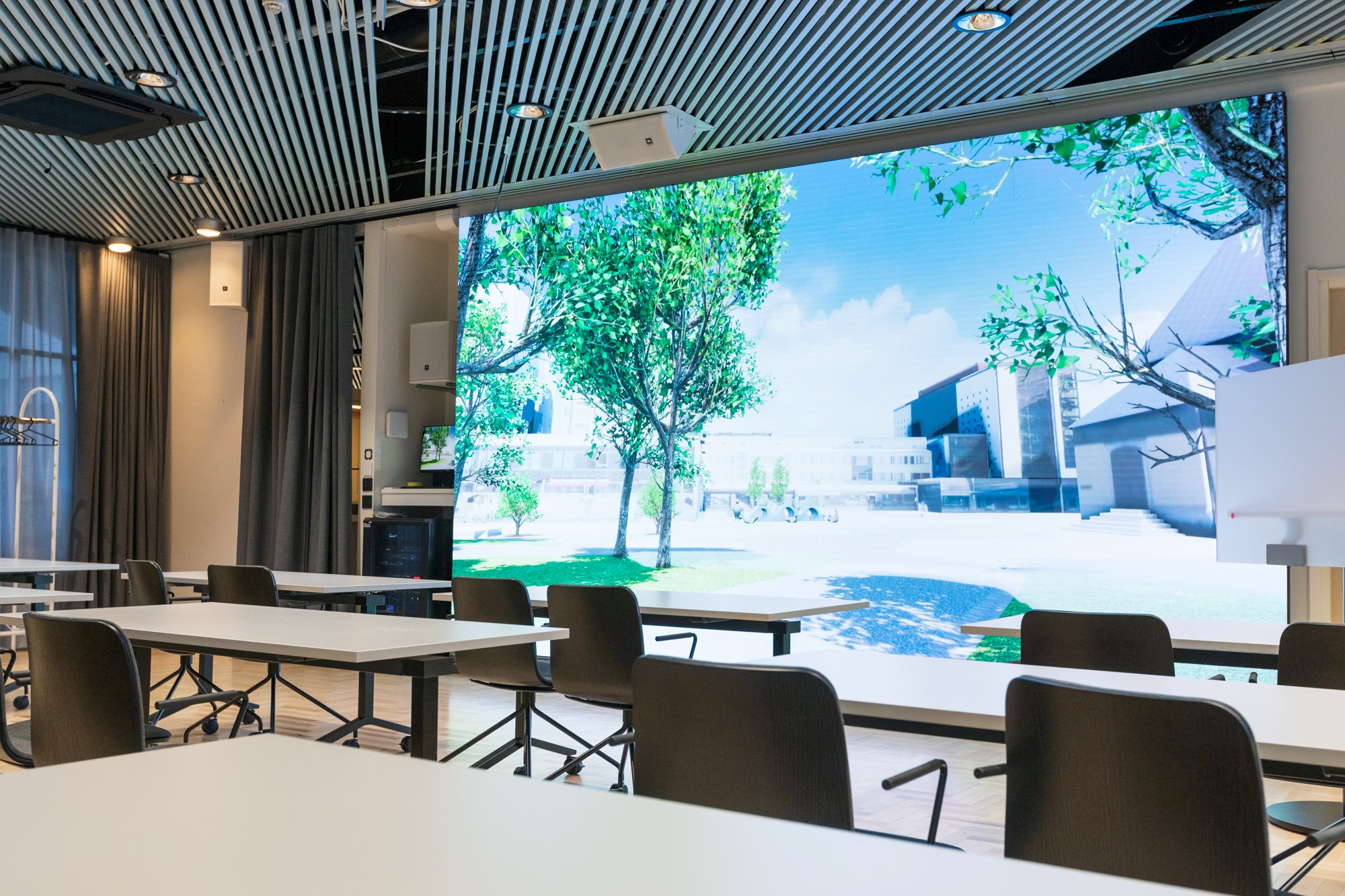 Venla-kokoushuone, jossa pöytiä ja tuoleja sekä suuri näyttö.