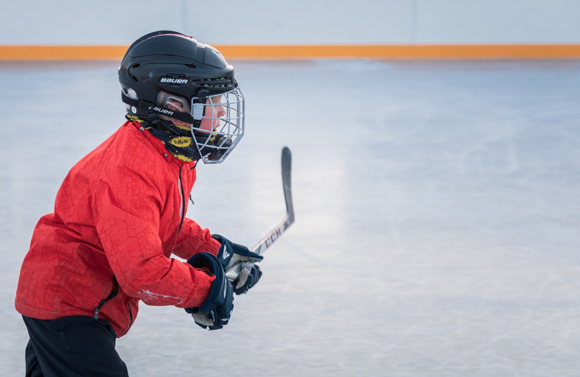 Lapsi luistelee jäällä maila kädessä ja kypärä päässä.