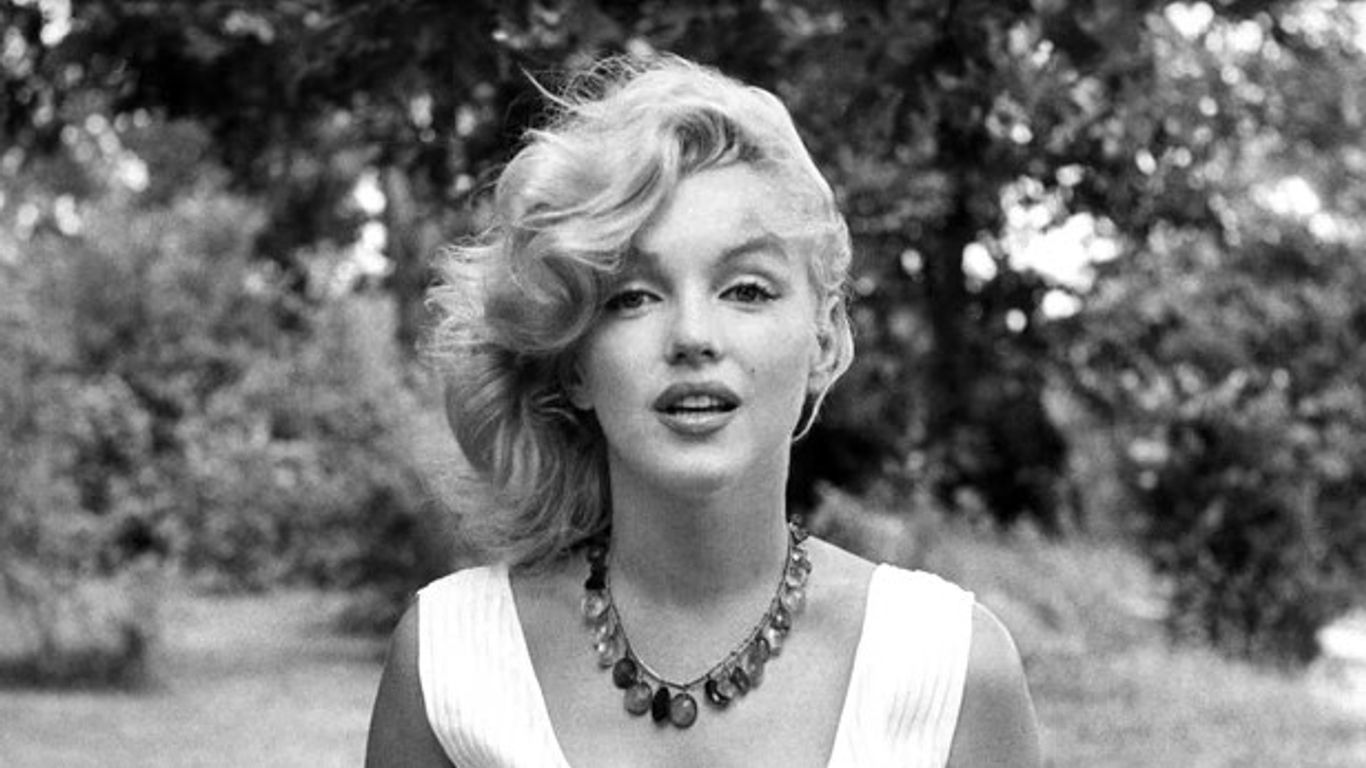 Näyttelijä Marilyn Monroe kuvattuna puuston edustalla.