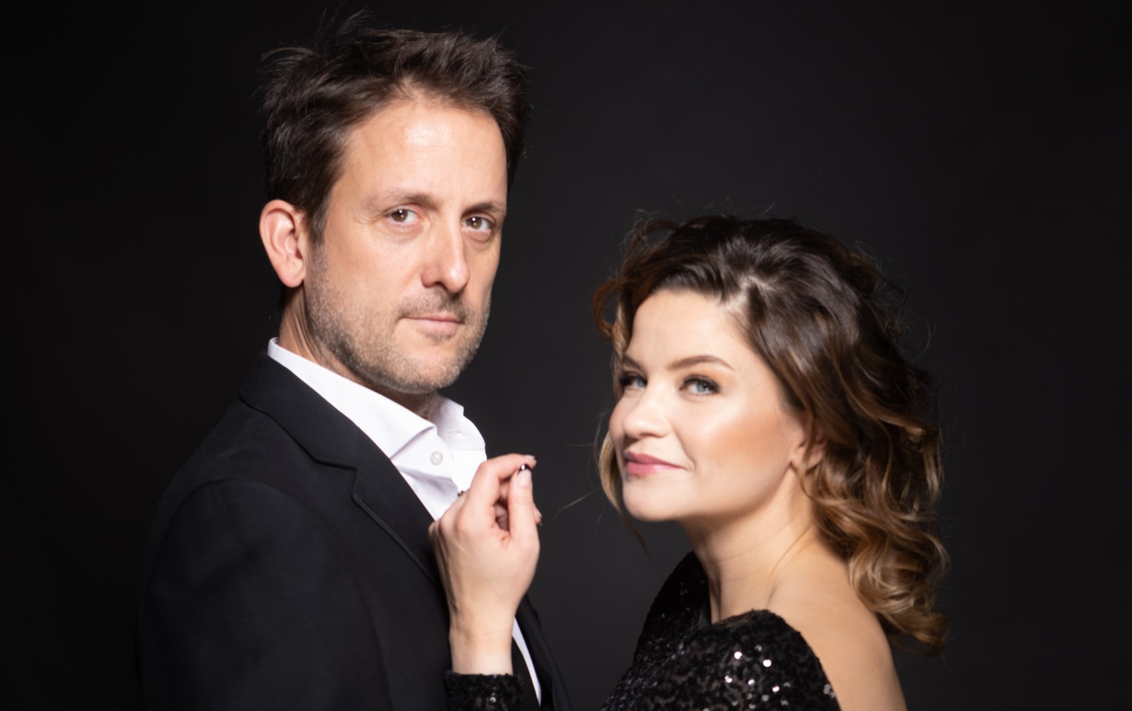 Juhlavasti pukeutuneet mies ja nainen seisovat toisiaan vasten ja katsovat kameraan.