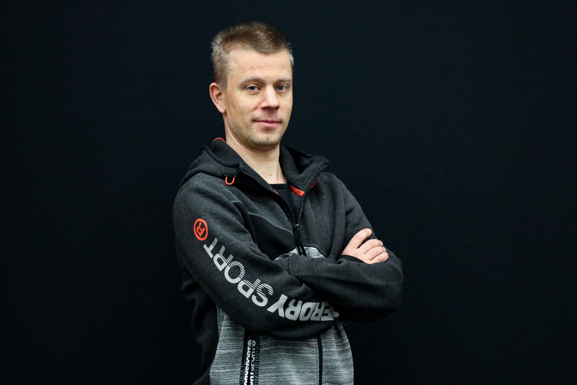 Antti Silvennoinen seisoo mustaa taustaa vasten kädet ristissä ja katsoo kameraan.