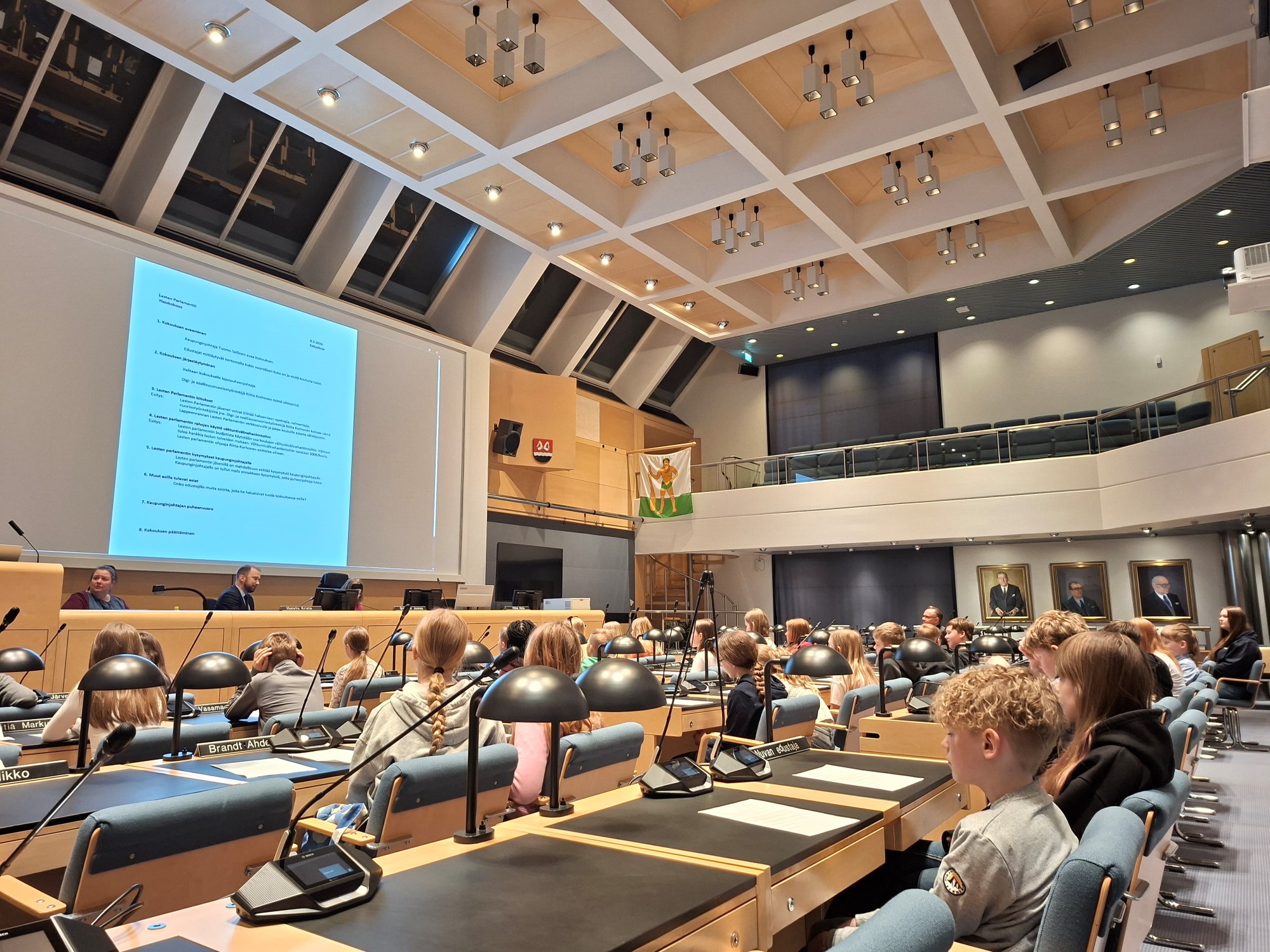 Lasten parlamentin jäseniä kokoontuneena Lappeenrannan valtuustosaliin, salin etuosassa kaupunginjohtaja Tuomo Sallinen avaa kokouksen.