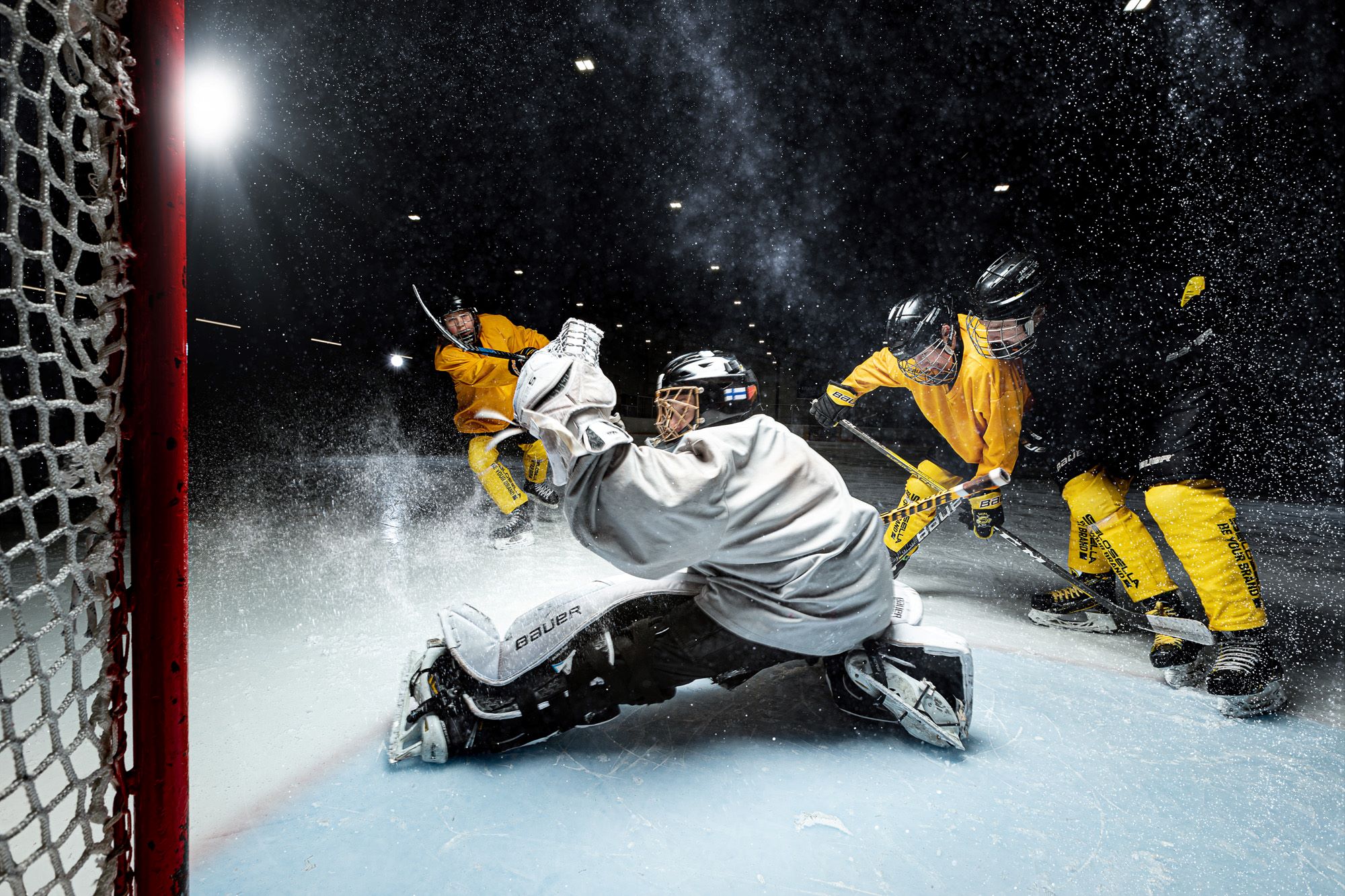 3 jääkiekkoilijaa ja maalivahti maalin edustalla jääkiekkokentällä.