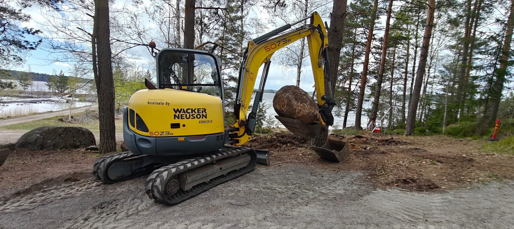 Telakaivurin kauhassa iso kivi virkistysreitin kunnostustyömaalla Saimaan rannalla.
