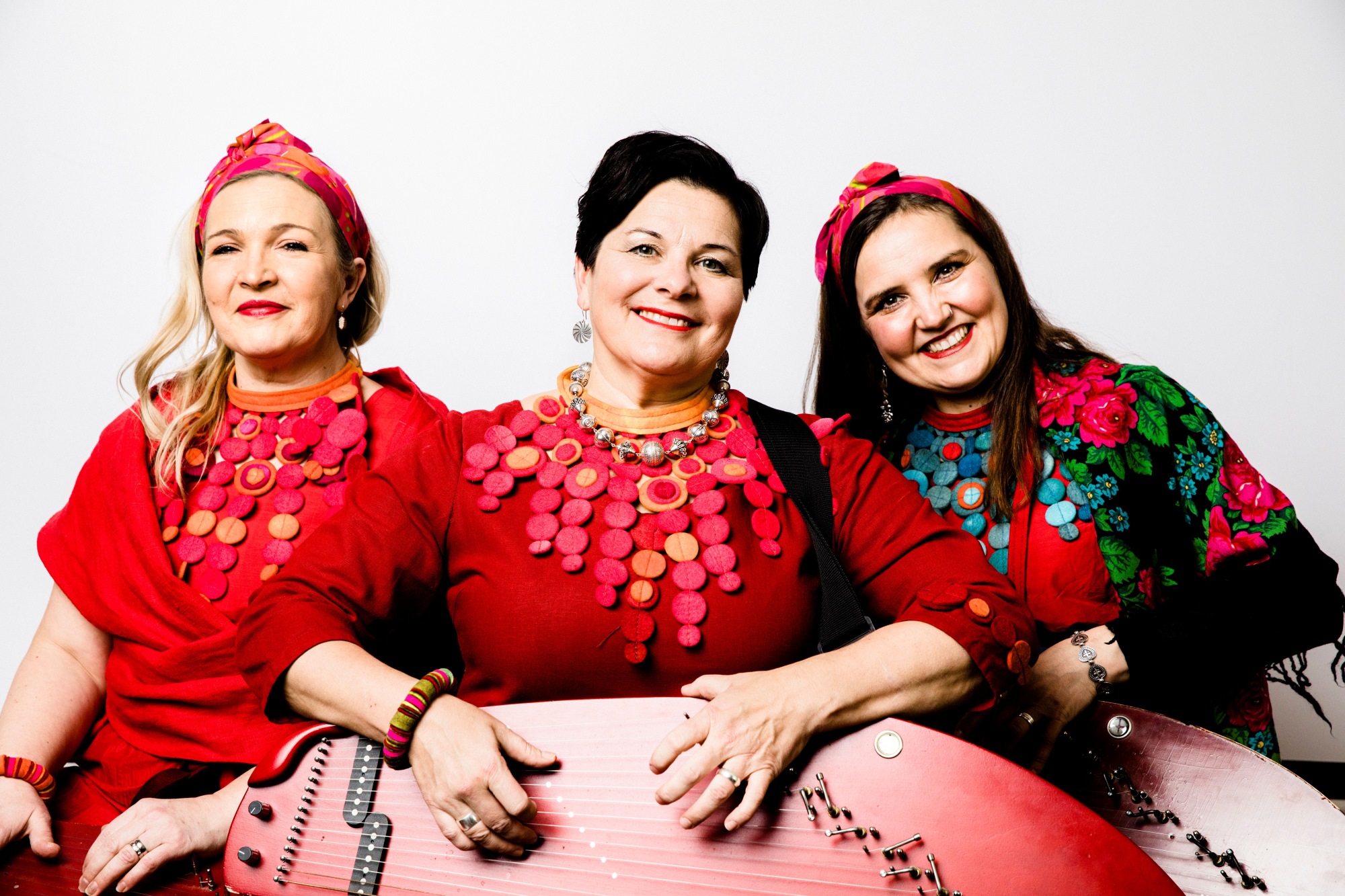 Set'akat yhtyeen kolme jäsentä perinneasuissa, keskimmäisellä kantele sylissään.