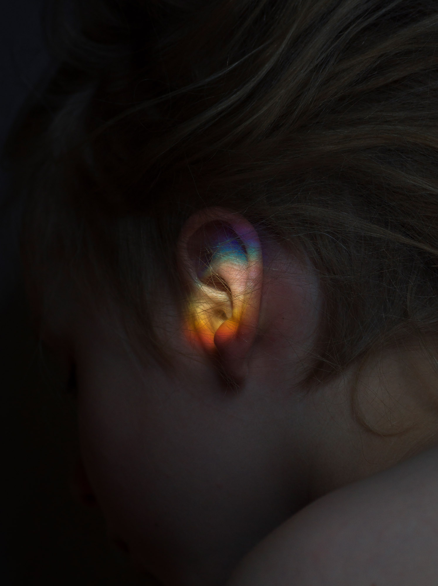 Pimeässä otettu valokuva ihmisen korvasta, johon heijastuu eri värisiä valoja.