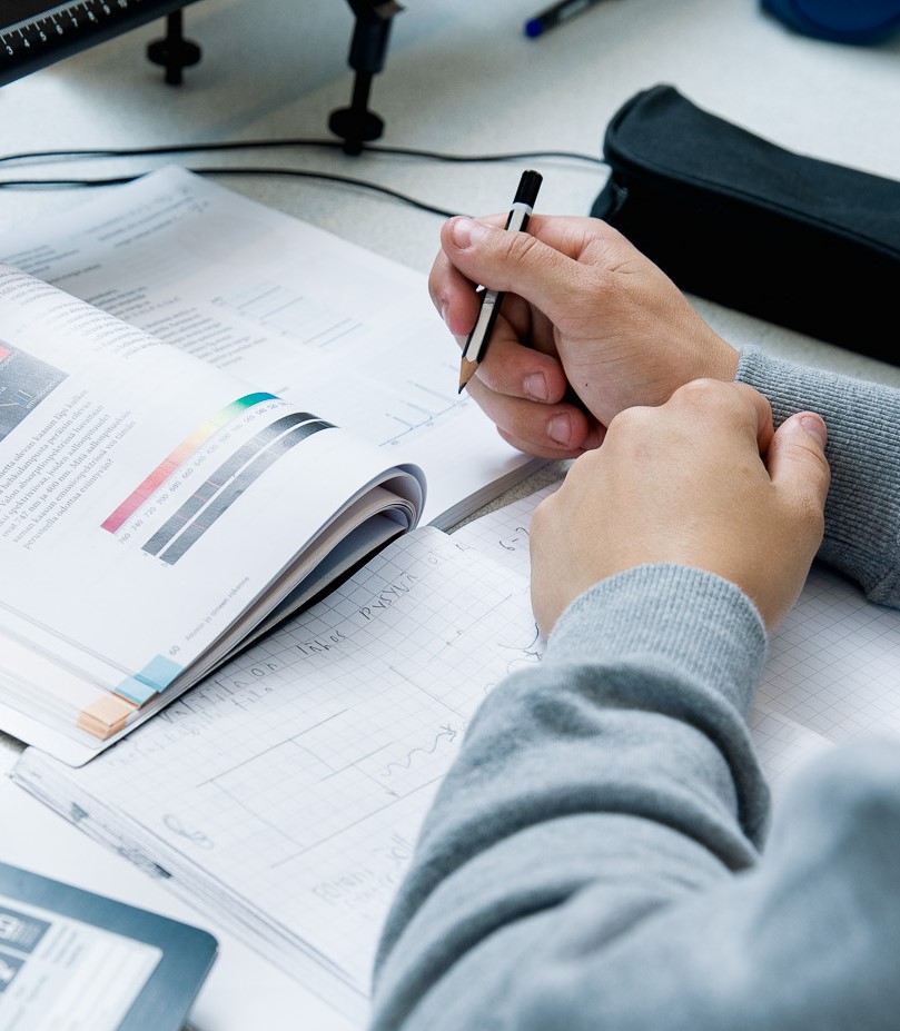 Oppilaan kädet tekemässä muistiinpanoja vihkoon.